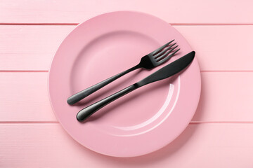 Ceramic plate with cutlery on pink wooden table, top view