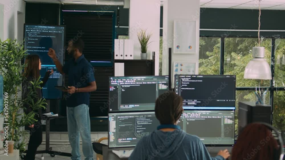  diverse team of software engineers analyzing code on wall screen tv, using digital tablet and workin