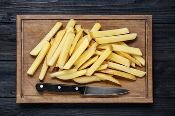 Cut raw potatoes on black wooden table, top view