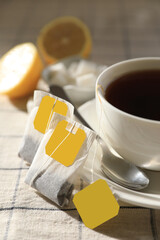 Tea bags near cup of hot drink on table, closeup - obrazy, fototapety, plakaty
