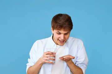 man holding pill and glass of water on blue background
