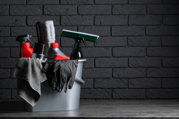 Different car cleaning products in bucket on table near black brick wall, space for text