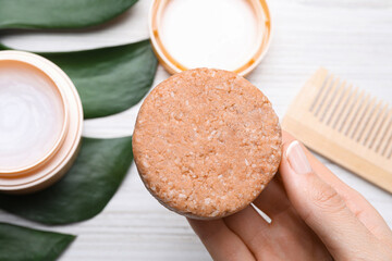 Woman holding solid shampoo bar at light wooden table, closeup. Hair care