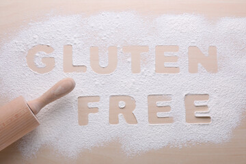 Rolling pin and phrase Gluten free written with flour on wooden table, flat lay