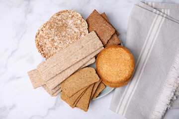 Rye crispbreads, rice cakes and rusks on white marble table, flat lay
