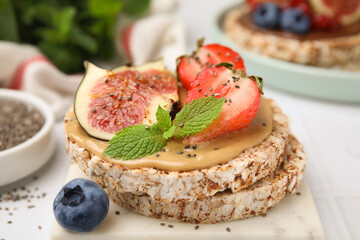 Tasty crispbreads with peanut butter, figs and berries on light table, closeup