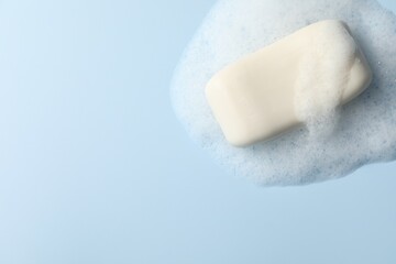 Soap with fluffy foam on light blue background, top view. Space for text