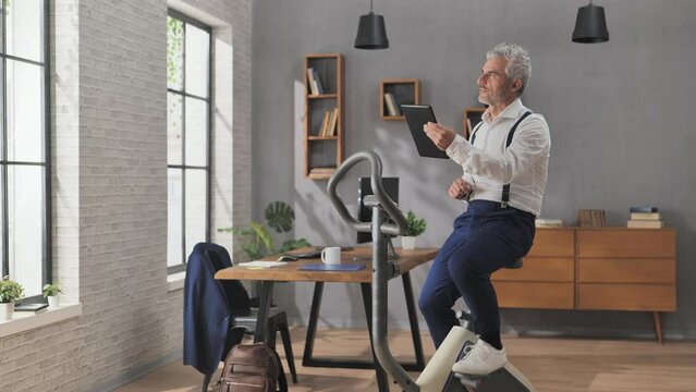 recreation in office,businessman takes work break,exercise bicycle and browsing scrolling on tablet
