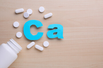Paper symbol Ca (Calcium), medical bottle and pills on violet background, top view
