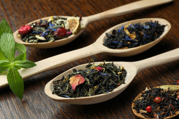 Spoons with dried herbal tea leaves on wooden table, closeup