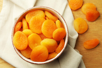 Tasty apricots with bowl on wooden table, flat lay. Dried fruits