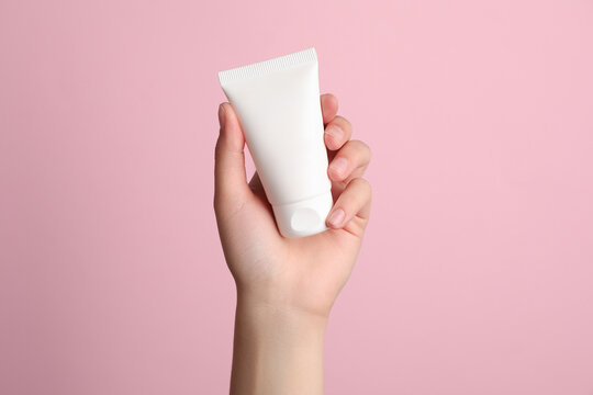 Woman holding tube of face cream on pink background, closeup
