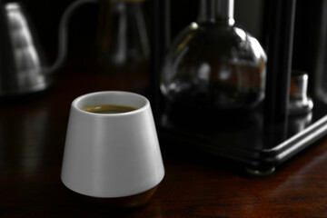 Cup with coffee and vacuum maker on wooden table in cafe