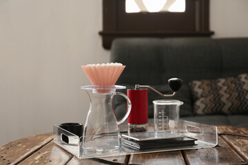 Manual coffee grinder with beans, glass jug and wave dripper on wooden table in cafe