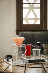 Manual coffee grinder with beans, glass jug and wave dripper on wooden table in cafe