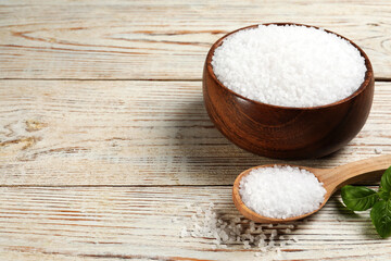 Bowl and spoon with natural sea salt on white wooden table. Space for text