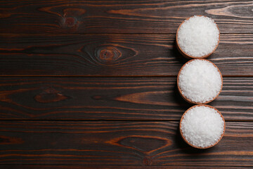 Bowls with natural sea salt on wooden table, flat lay. Space for text
