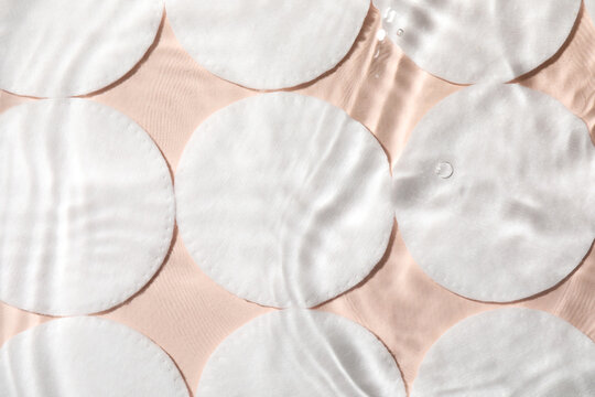 Many cotton pads in water on beige background, flat lay