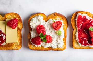 Open Sandwiches fro tasty breakfast with Brioche bread slices, ricotta cheese, butter, fresh raspberries and raspberry jam and mint leaves