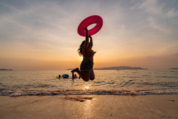 Silhouette happy fat girl having fun on summer vacation playing colorful rubber ring with sunset...