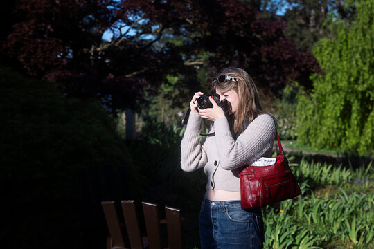 Girl with a modern fullframe compact camera taking pictures in a park 