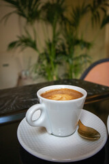 White porcelain coffee cup with cappuccino drink on black marble table in cafe.