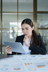 Portrait of a thoughtful Asian businesswoman looking at financial statements and making marketing plans using a tablet computer on her desk