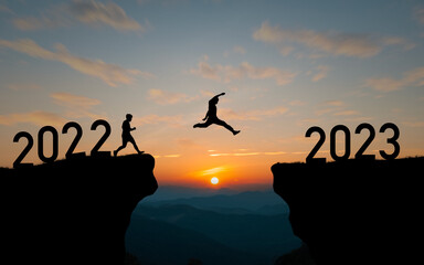 Silhouette man jumping from 2022 cliff to 2023 cliff with cloud sky and sunlight and happy new year...