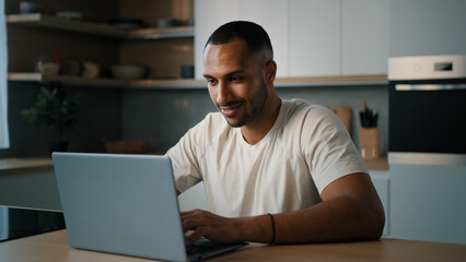 Smiling African millennial man guy American male user freelancer at home kitchen finish distant work with laptop satisfied with computer app online website networking shopping looking at camera smile