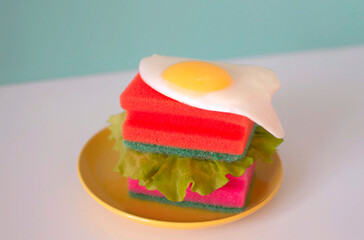 Modern still life. Creative sandwich with hygienic sponges and chicken egg on yellow plate with kitchen sponges. Creative idea. Concept of household hygiene