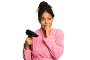 Young brazilian woman wearing a pink bathrobe holding an hairdryer isolated biting fingernails, nervous and very anxious.