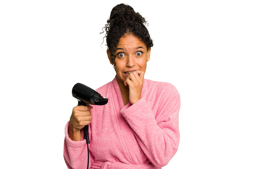 Young brazilian woman wearing a pink bathrobe holding an hairdryer isolated biting fingernails, nervous and very anxious.