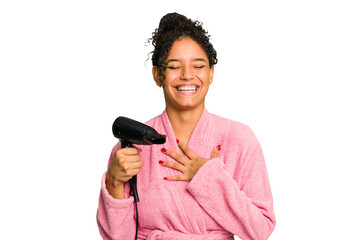 Young brazilian woman wearing a pink bathrobe holding an hairdryer isolated laughs out loudly...