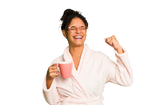 Young brazilian woman wearing a pajama holding a cup isolated raising fist after a victory, winner concept.