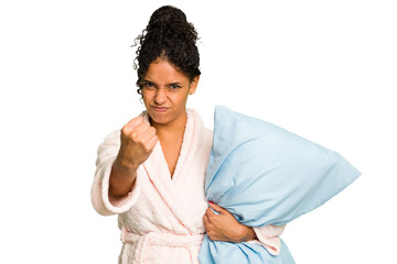 Young brazilian woman wearing a pajama holding a pillow isolated showing fist to camera, aggressive...