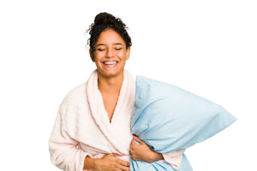 Young brazilian woman wearing a pajama holding a pillow isolated laughing and having fun.