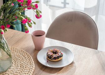 Cozy breakfast. Cup of coffee, pink donut and flowers on the table. Weekend breakfast, relax, girls time