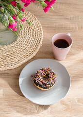 Cozy breakfast. Cup of coffee, pink donut and flowers on the table. Weekend breakfast, relax, girls time