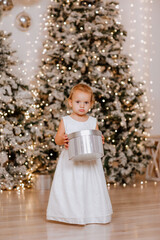 Girl in white evening dress is posing with silver present in Christmas studio