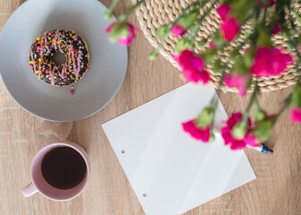 Cozy breakfast and planning. Notepad and pen, cup of coffee, pink donut, flowers and candles on the table. Women's desktop. Top view