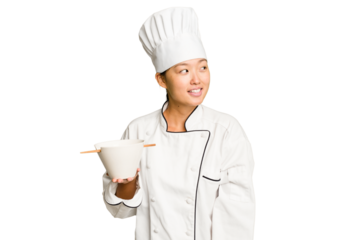 Young chef asian woman holding a bowl of ramen isolated looks aside smiling, cheerful and pleasant.