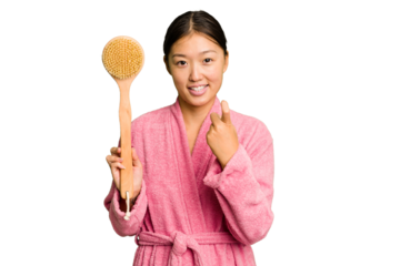 Young asian woman holding a shower brush isolated pointing with finger at you as if inviting come closer.