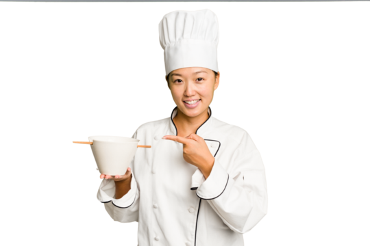 Young chef asian woman holding a bowl of ramen isolated smiling and pointing aside, showing something at blank space.