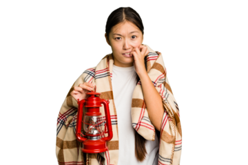 Young asian woman wearing a blanket and holding a lamp isolated biting fingernails, nervous and very anxious.