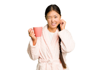 Young asian woman wearing a pajama holding a cup isolated covering ears with hands.