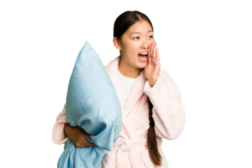 Young asian woman wearing a pajama holding a pillow isolated shouting and holding palm near opened mouth.