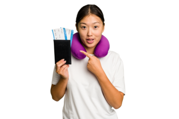 Young asian woman with inflatable travel pillow on her neck holding passport isolated pointing to the side
