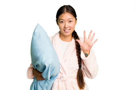 Young asian woman wearing a pajama holding a pillow isolated smiling cheerful showing number five with fingers.