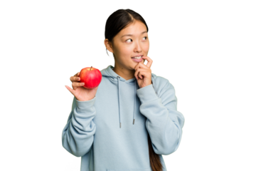 Young asian woman holding a red apple isolated relaxed thinking about something looking at a copy space.