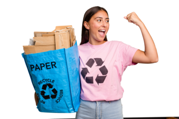 Young caucasian woman holding a recycling bag full of paper to recycle isolated raising fist after a victory, winner concept.